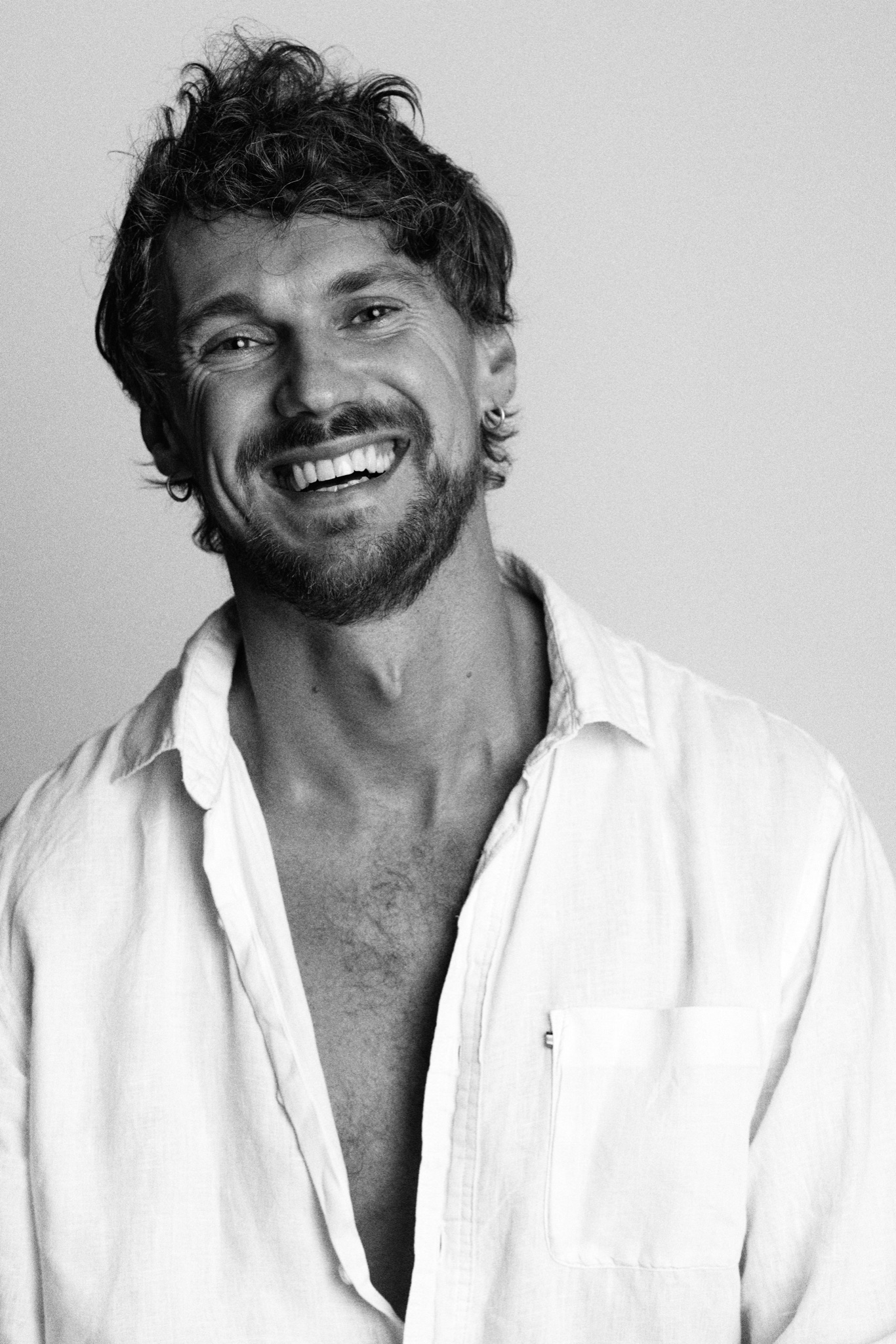 Black-and-white portrait of Damian Kalusiewicz smiling in a white shirt.