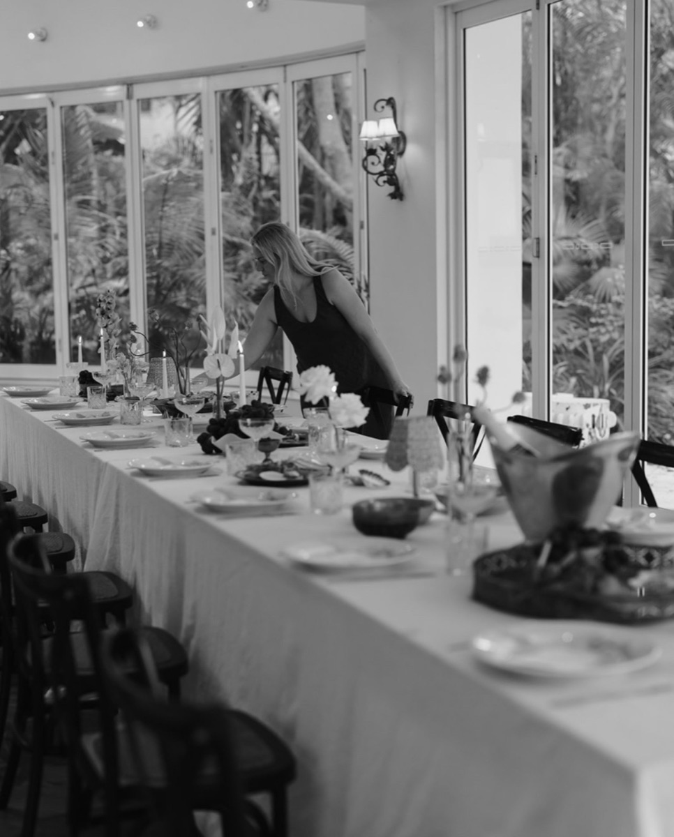 Black-and-white photograph of Katie Day arranging a long table setting.